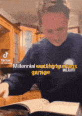 a man in a blue sweater is reading a book with the words millennial watching hashtags garage in yellow letters