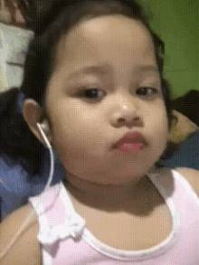 a little girl wearing headphones and a pink tank top is making a funny face .