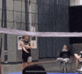 a group of people are playing volleyball in a gym with a net in the foreground .