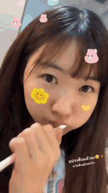 a girl is brushing her teeth with stickers on her face including a smiley face