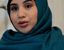 a woman wearing a blue hijab is making a face .
