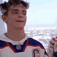 a young man wearing a hockey jersey and a headband is looking at the camera .
