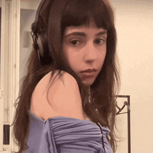 a woman wearing headphones and a blue shirt looks at the camera