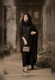 a woman in a black dress and hijab is standing in front of a building
