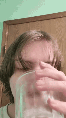 a young man drinking from a glass with his hand on his face