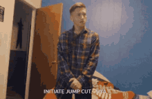 a man in a plaid shirt is standing in a bedroom and says initiate jump cut hya