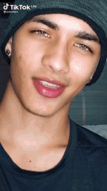 a young man wearing a black shirt and a green beanie has a tiktok lite watermark on his face