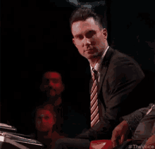 a man in a suit is standing in a dark room holding a red object in his hand .