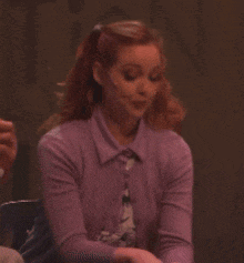 a woman wearing a purple sweater is sitting in front of a newspaper
