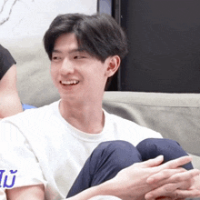 a man in a white shirt is sitting on a couch with his legs crossed and smiling