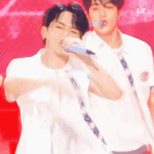 a man in a white shirt is singing into a microphone while another man stands behind him .