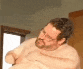 a shirtless man with a beard and glasses is sitting on a chair .