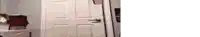 a white door with a black handle is open in a room with a white wall .