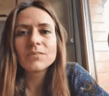 a woman with long brown hair is wearing a blue shirt and looking at the camera