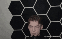 a young man wearing headphones stands in front of a black and white hexagon wall