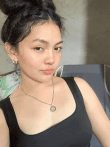 a woman wearing a black tank top and a silver necklace with a coin on her chest
