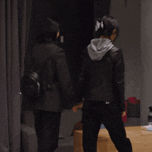 a woman in a black jacket with a hood is standing next to another woman in a black jacket