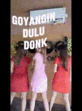 three women are standing in front of a wall that says goyangin dulu donk on it