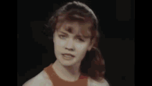 a woman in an orange tank top is dancing in front of a white wall .