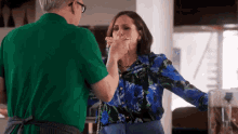 a man in a green shirt is feeding a woman in a blue shirt .