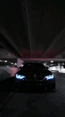 a black bmw is parked under a bridge in a dark parking garage