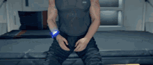 a man is sitting on a bed with his hands on his hips and a watch on his wrist .