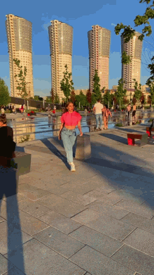 a woman in a pink crop top stands in front of a row of tall buildings