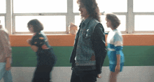 a man wearing a denim vest with the letter a on it stands in a hallway with other people