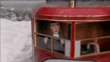 a cartoon man is driving a red bus in the snow .