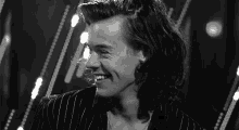 a black and white photo of a young man with long hair smiling .