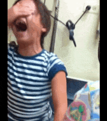 a little girl in a striped shirt is covering her eyes with her hand .