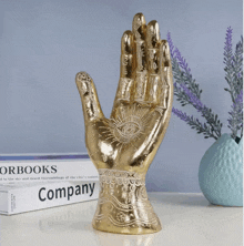 a statue of a hand with an eye on it sits next to a book titled company