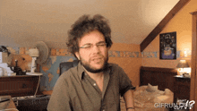 a man with glasses and a beard is sitting in front of a keyboard and a poster that says what the f