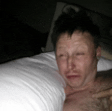 a man without a shirt is laying in bed with his eyes closed .