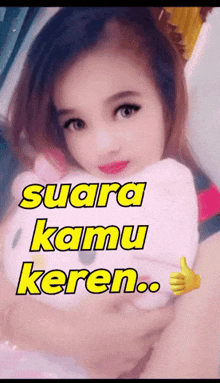 a girl holding a hello kitty stuffed animal with the words suara kamu keren written above her