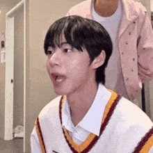a young man wearing a white shirt and a striped vest is making a funny face