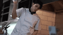 a young man in a chef 's uniform is standing in a kitchen holding a pan .