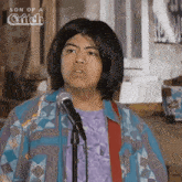a man in a wig is singing into a microphone in front of a sign that says son of a bitch