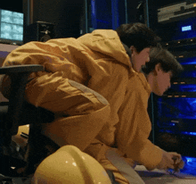 a man in a yellow jacket sits on a chair next to a yellow helmet