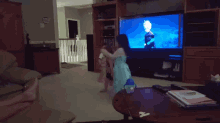 a little girl in a blue dress is dancing in front of a tv screen