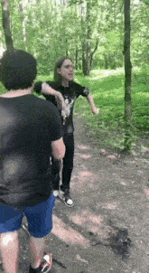 a man in a black shirt is standing next to another man in blue shorts in the woods .