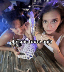 two women are sitting at a table with the words je suis toute ouie on the bottom