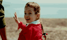 a little girl in a red jacket is smiling and waving at the camera