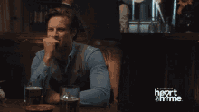 a man sits at a table with a glass of beer in front of a sign that says super channel heart & me