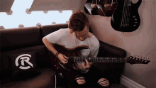 a man playing a guitar on a couch with a pillow that says r on it