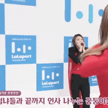 a woman is singing into a microphone in front of a wall that says lalaport yokohama on it .