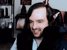 a man with long hair and a beard is smiling in front of a picture of a couple