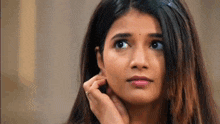 a woman is touching her ear with her hand and looking up .