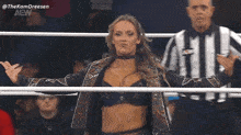 a woman stands in a wrestling ring with her arms outstretched and a referee behind her