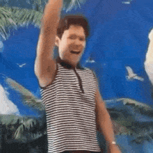 a man in a striped tank top is standing in front of a blue wall with his arm in the air .